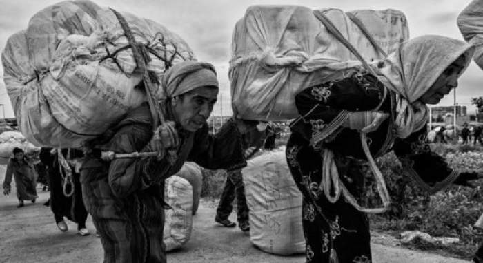 Two women walk towards the border with two heavy loads on their